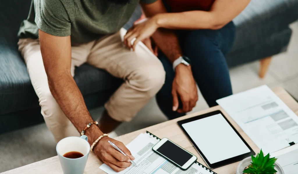 A couple engaged in financial planning, sitting on a couch and writing on a tablet.