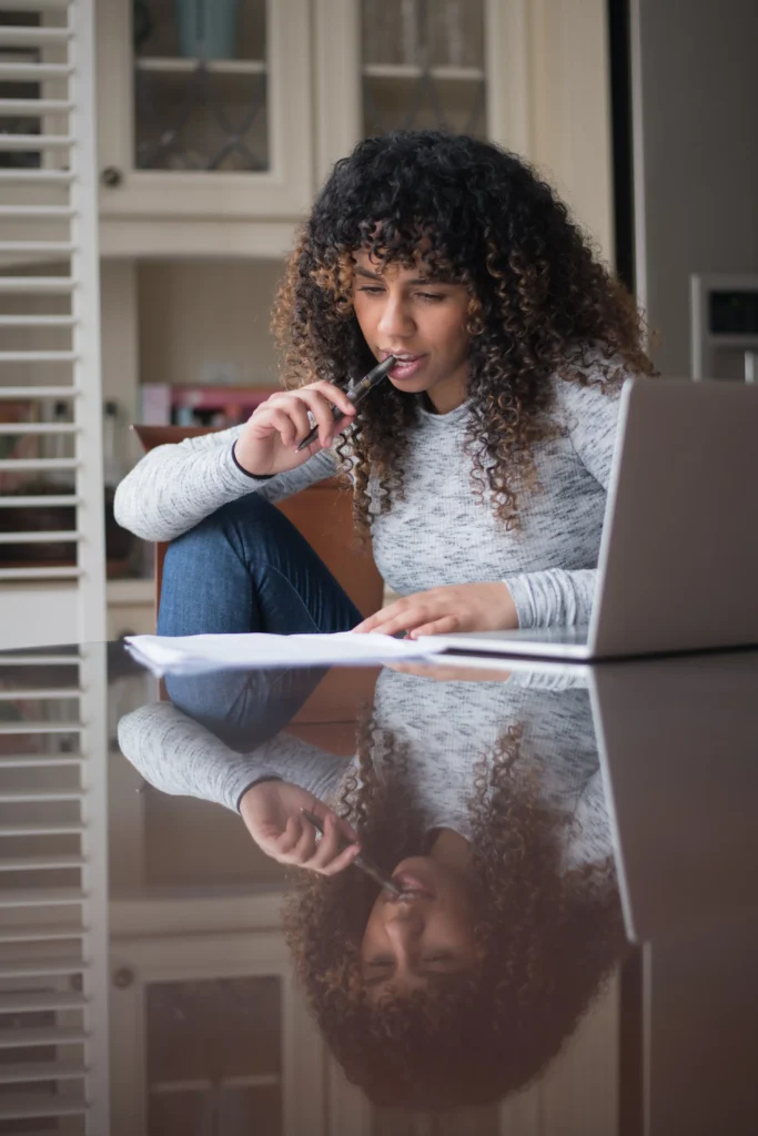 A woman sitting at a table with a laptop and a pen.