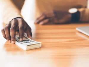 A hand holding a stack of money on a desk.