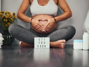 A pregnant woman sitting cross legged with her hands on her stomach.