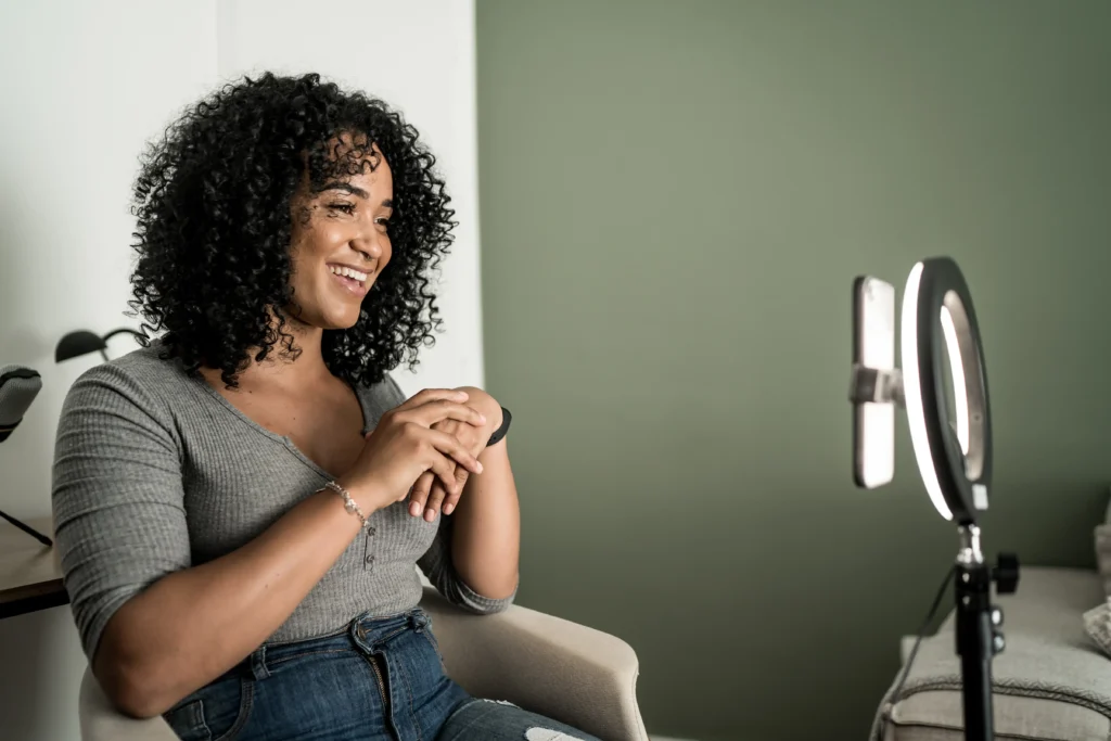 A woman with curly hair sitting in front of a camera.