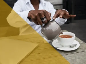 A woman pouring tea into a cup on a table.