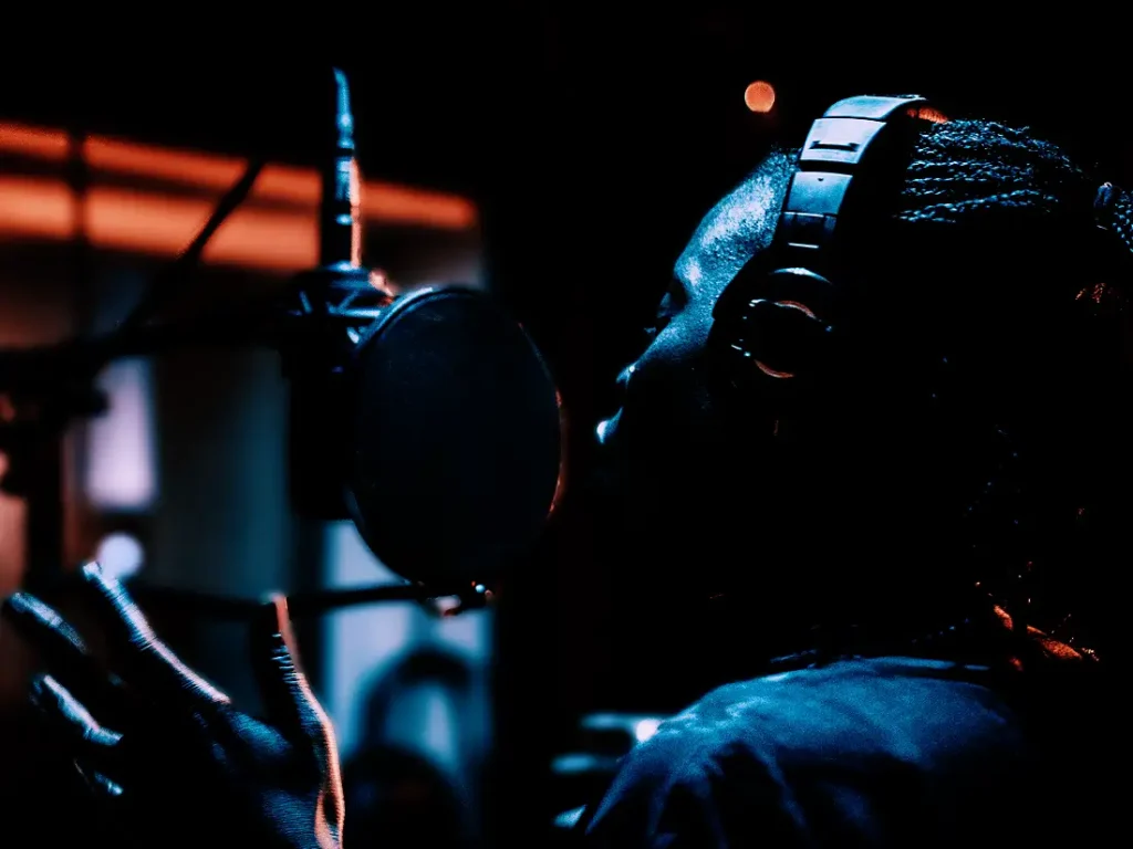 Silhouetted figure recording vocals in a dimly lit studio.