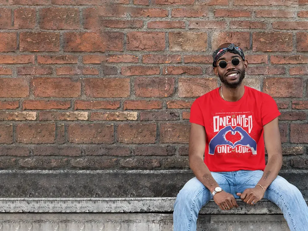 Man smiling and sitting on a ledge in front of a brick wall.