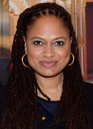 A woman with medium-length braided hair and hoop earrings, smiling at the camera.