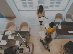 Overhead view of an office lobby with an intern standing and reading a document while two others walk by quickly.