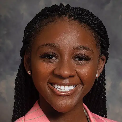 Portrait of a smiling black woman wearing a pink shirt and pearl earrings, against a grey background.