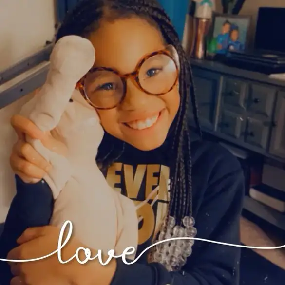 Girl with glasses embracing a plush toy with the word "love" inscribed below.
