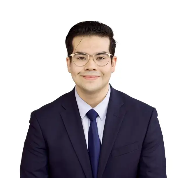 A professional portrait of a man wearing glasses, a blue suit, and a light blue shirt, smiling at the camera against a white background.