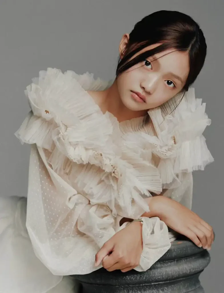 A person in a ruffled, translucent white blouse with a thoughtful expression.