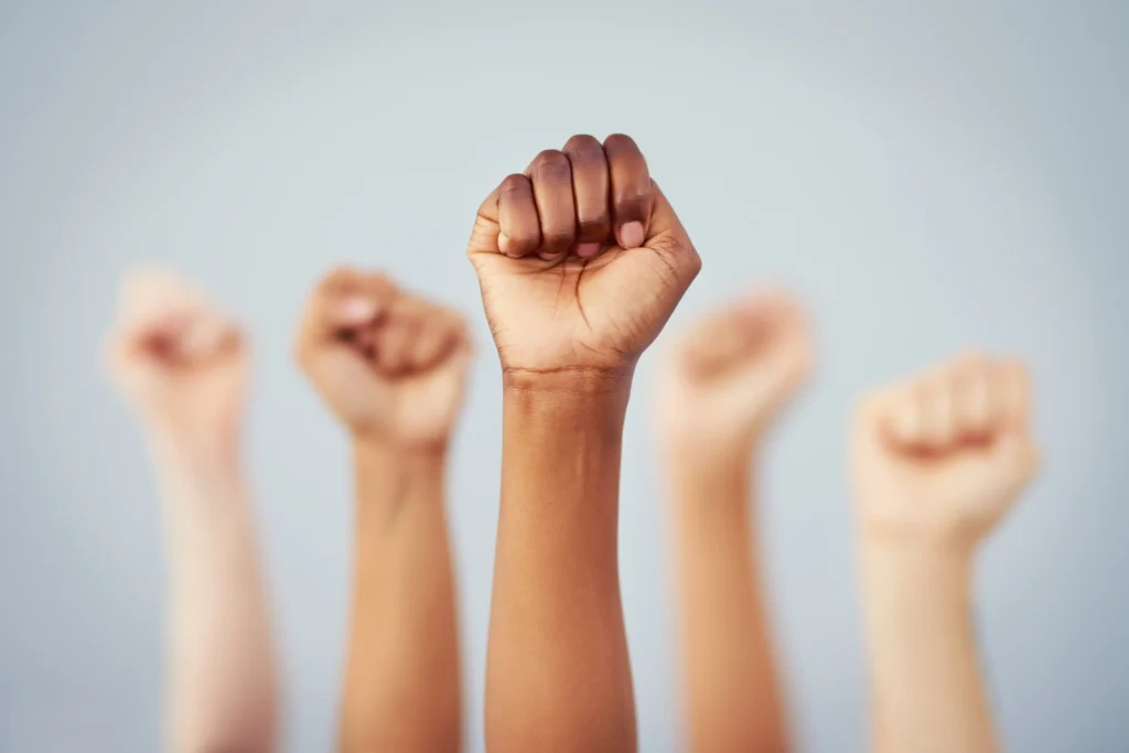 Five clenched fists raised against a light blue background, signifying unity.