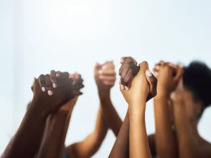 A group of people holding hands up together against a light background, showing unity and solidarity.