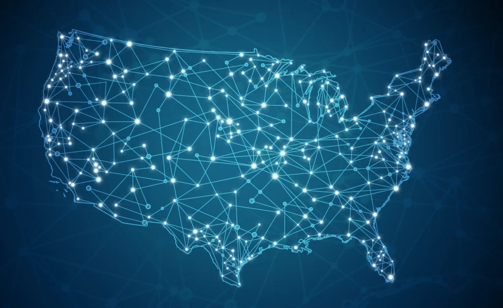 An illuminated, abstract outline of the United States map is formed by a network of interconnected white dots and lines against a dark blue background, suggesting widespread connectivity.