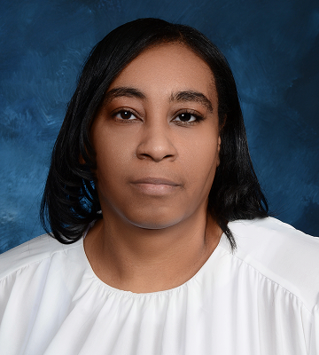 A woman with straight black hair, wearing a white blouse, poses in front of a blue studio backdrop.