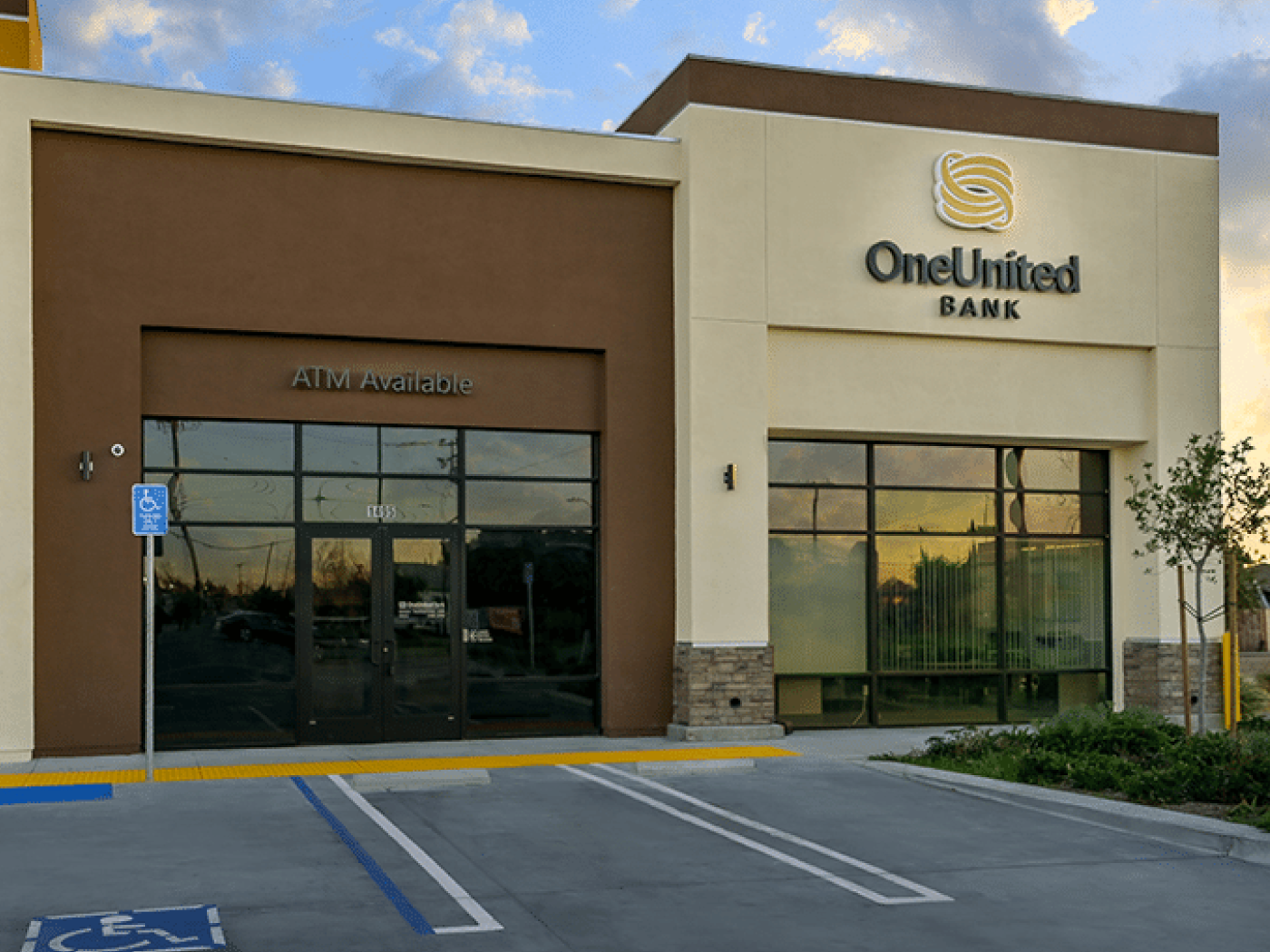 Exterior view of a OneUnited Bank branch with large windows, an ATM, and adjacent accessible parking spaces.