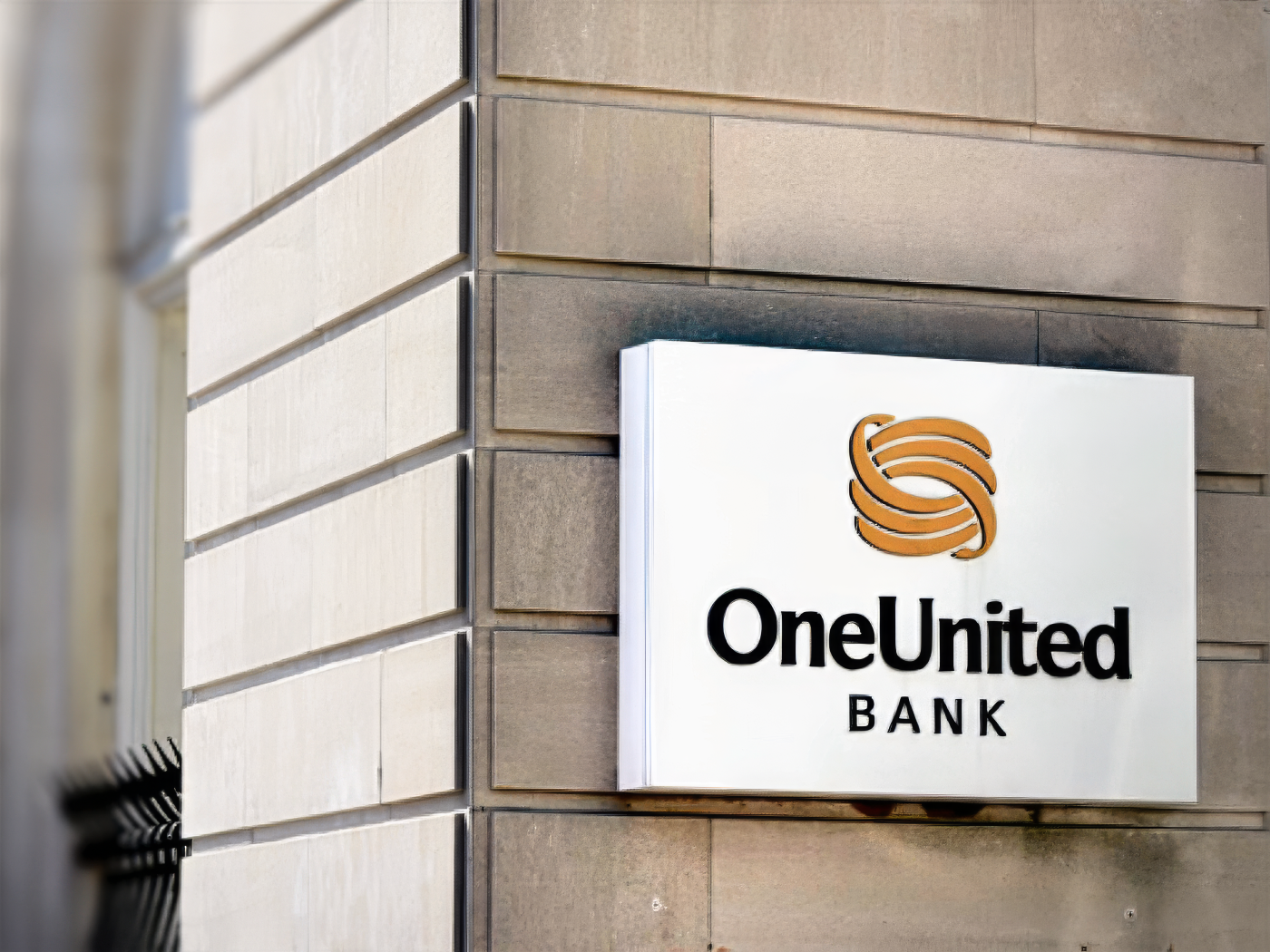 A sign reading "OneUnited Bank" with a gold logo is mounted on the corner of a stone building.